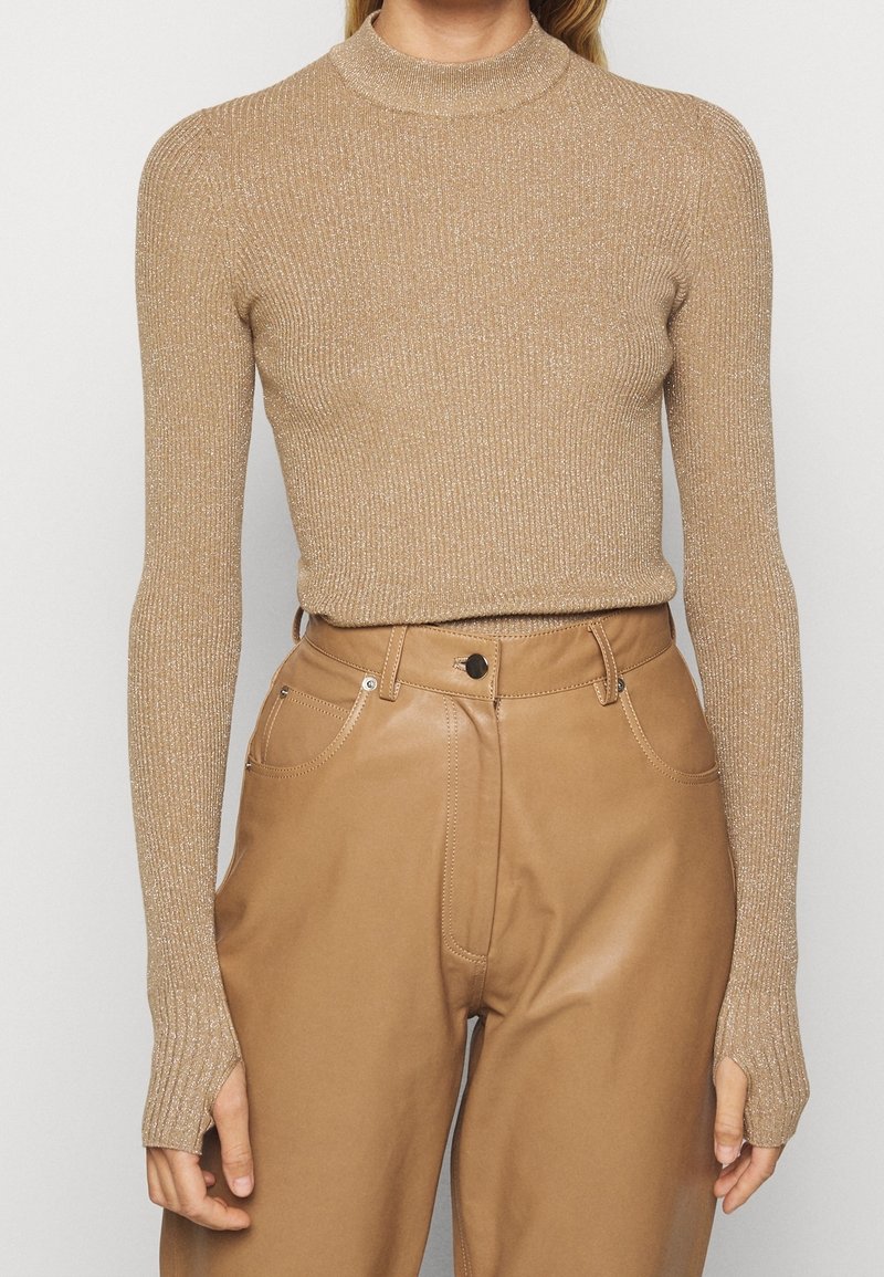 Femme portant un pull col roulé beige moulant à manches longues et côtelé, associé à un pantalon en cuir camel taille haute.