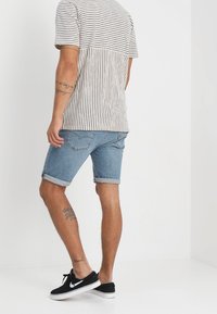 Pruhovaná košile s krátkým rukávem v bílé a černé barvě, doplněná modrými denimovými kraťasy. Tenisky jsou černé s bílými detaily. Neformální letní outfit.