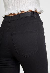 Vaqueros de mezclilla negra con un corte ajustado, que presentan bolsillos traseros con detalles de costura y una textura suave. La cintura tiene una etiqueta negra.