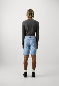 Mørk langermet skjorte kombinert med lyseblå denimshorts, med baklommer og rett ben-design. Bært med svarte joggesko og hvite sokker.