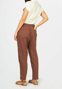 Browna linbyxor med en avslappnad passform, elastisk midja, sidofickor och en mjuk textur, i kombination med tanfärgade, flätade sandaler.