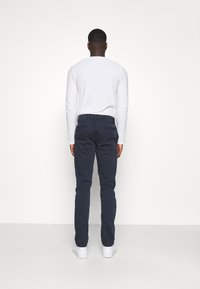 Mörkblå chinos med slim fit, bomullstyg, knapp- och dragkedja, samt bakfickor. Kombineras med en vit långärmad skjorta och vita sneakers.