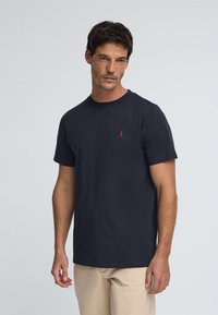 T-shirt in cotone blu navy con scollo rotondo e maniche corte; presenta un piccolo logo rosso sul petto a sinistra.