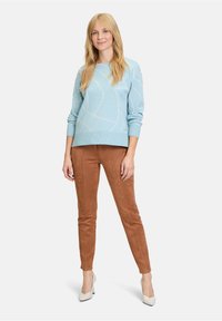 Lichtblauwe trui met een geometrisch crèmekleurig patroon en geribbelde boorden, gecombineerd met bruine suède broek en witte hakken.