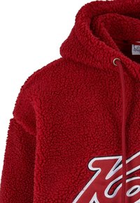 Sweat à capuche en sherpa polaire rouge avec un grand motif partiel de lettre rouge avec contour blanc et capuche avec cordon et œillets en métal.