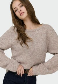Pull en maille mauve avec une coupe décontractée, des manches larges et un col arrondi. La texture visible ajoute de la douceur. Associé à un denim foncé.