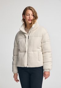 Padded jacket w jasnym kremowym kolorze, wykonany z miękkiego materiału. Posiada wysoki kołnierz, zamek błyskawiczny oraz boczne kieszenie. Lekko skrócony krój.