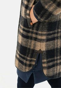 ruitjes wollen blend jas in beige en marineblauw, met zijzakken en een splitzoom, voorzien van leren accenten en een zachte textuur.