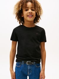 T-shirt noir à manches courtes avec un petit logo, associé à un jean en denim bleu et une ceinture noire. La texture semble lisse et décontractée.