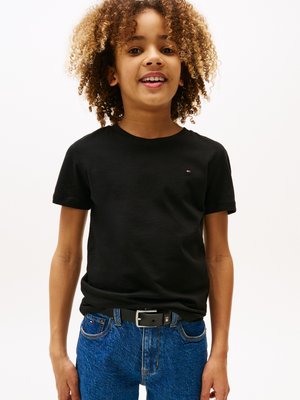 T-shirt noir à manches courtes avec un petit logo, associé à un jean en denim bleu et une ceinture noire. La texture semble lisse et décontractée.