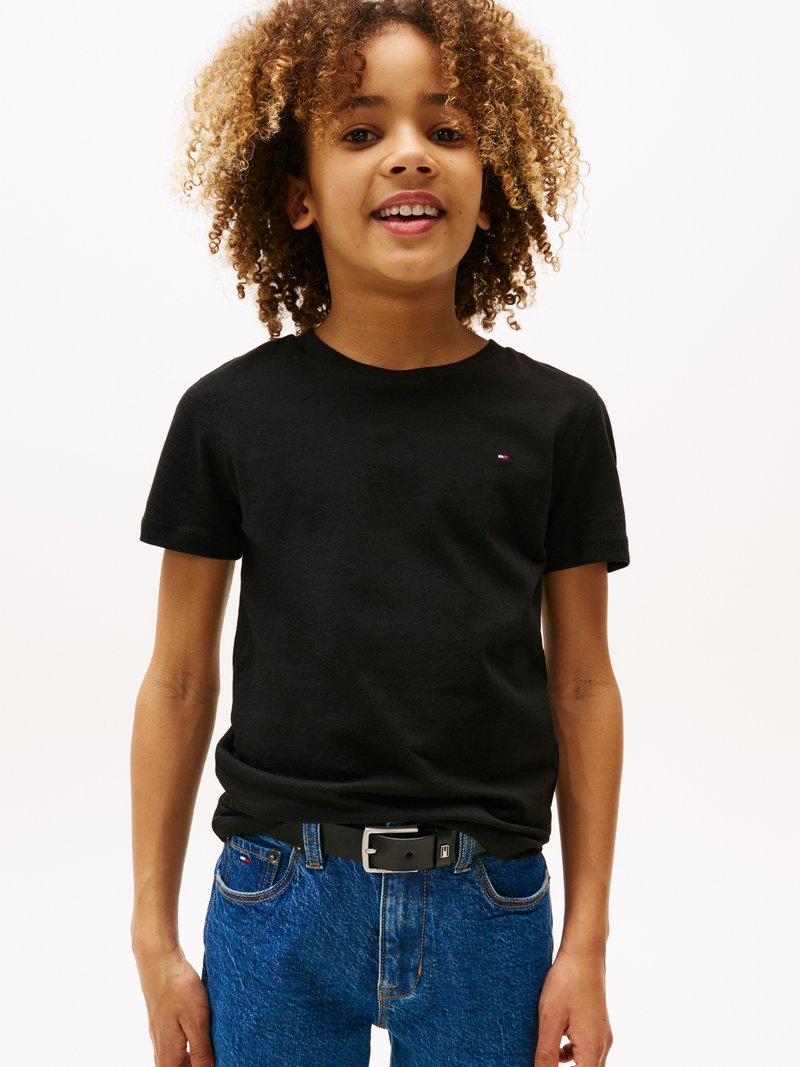 T-shirt noir à manches courtes avec un petit logo, associé à un jean en denim bleu et une ceinture noire. La texture semble lisse et décontractée.