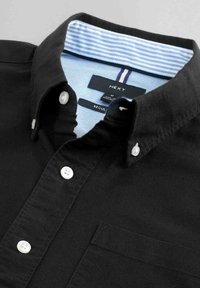 Camisa de algodón negra con cuello abotonado, botones blancos y interior del cuello a rayas en azul claro. Incluye un bolsillo en el pecho.