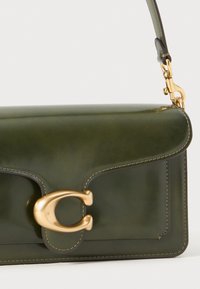 Dark green leather handbag with a gold-tone clasp, detailing in cream stitching, and a detachable shoulder strap. Smooth texture.
