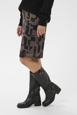 Brown patterned pencil skirt featuring geometric black designs, paired with knee-high black leather boots with decorative buckles and a low heel.
