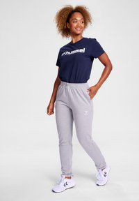 Marineblå t-shirt med hvid "hummel" logo, grå sweatpants med logo på venstre ben og hvide sportssko med sorte detaljer.