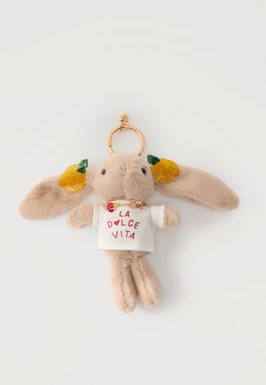 Blød beige kanin-nøglering iført hvid "La Dolce Vita" t-shirt med gule frugtdekorationer på ørerne og en guldring som vedhæng.