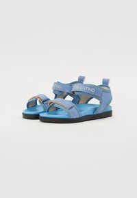 Blauwe stoffen sandalen hebben een dubbelriemontwerp met klittenbandsluitingen, een gevoerde blauwe binnenzool en een vlakke zwarte rubberen zool.