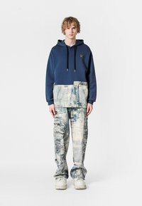 Sudadera con capucha en color azul marino con un panel inferior texturizado, combinada con pantalones de un azul grisáceo claro con un patrón, de corte holgado y puños elásticos.