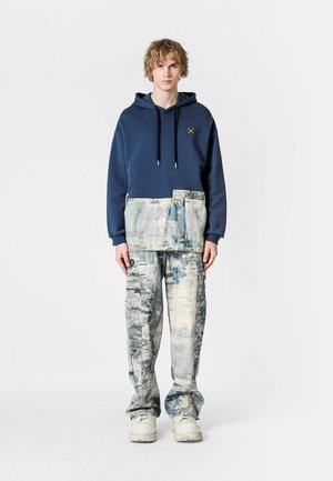 Sudadera con capucha en color azul marino con un panel inferior texturizado, combinada con pantalones de un azul grisáceo claro con un patrón, de corte holgado y puños elásticos.