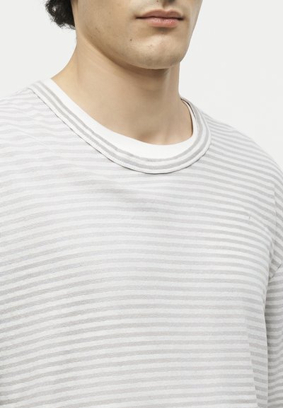 Κοντινό πλάνο ενός ατόμου που φοράει ένα ανοιχτό γκρι και λευκό ριγωτό μπλουζάκι με στρογγυλή λαιμόκοψη, εμφανιζόμενο από τον λαιμό έως το πάνω μέρος του στήθους.