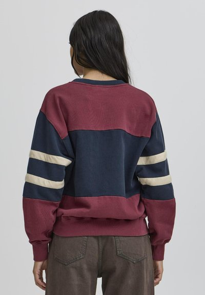 Burgundi, tumesinine ja kreemivalge laikelementidega pusakrunt pikkade varrukatega, millel on kreemilised triibud varrukatel ja soonikkoes mansetid. Pehme tekstuur.