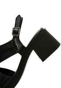 Zwarte sandaal met hak en een chunky, ribbelige hak. Beschikt over een leren bovenzijde, verstelbare enkelriem en een open teen ontwerp.