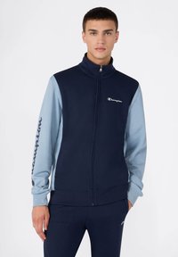 Chaqueta de cremallera azul marino y celeste con cuello alto, que presenta un logo en el pecho y un diseño de mangas en contraste. Textura suave.