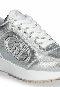 Sneaker argentato metallico con finitura testurizzata, lacci bianchi e logo circolare. Presenta una suola imbottita e dettagli lisci.