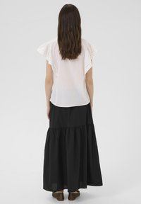 Blouse blanche avec des manches à volants et des détails brodés, associée à une longue jupe noire à volants, offrant une coupe décontractée et un tissu lisse.