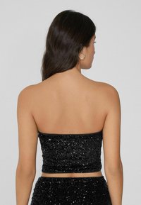 Zwarte pailletten crop top met een strapless ontwerp, featuring een aansluitende pasvorm en een gladde textuur. Achteraan is er een nette, naadloze afwerking te zien.
