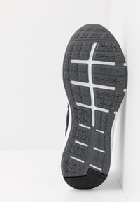 Černá a šedá podrážka tenisek Adidas s texturovaným gumovým povrchem, která má segmentovaný vzor a branding "adiwear" poblíž paty.