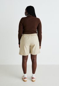 Top largo de manga larga ajustado en marrón combinado con pantalones cortos beige que cuentan con una cinturilla elástica. Los pantalones cortos son de largo hasta la rodilla, con una textura lisa y dobladillos.