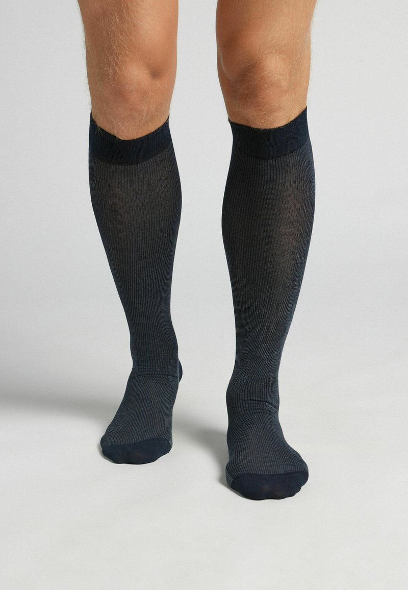 Mörkblå knälånga strumpor med ribbad struktur och släta manschetter, som har en jämn yta och en åtsittande design runt vaden.