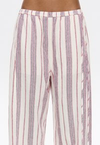 Pantalons en lin légers avec des rayures verticales rouges et bleues sur un fond crème. Taille élastique, coupe décontractée et texture douce.