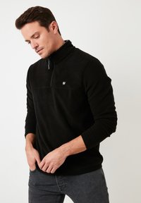 Pullover in pile nero con colletto alto, mezza zip e un piccolo logo sul petto. Presenta maniche lunghe e una trama morbida.