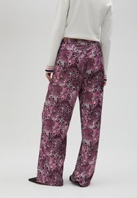 Purple leopard print trousers with a loose fit, featuring a smooth texture and wide leg design. Elastic waistband and side pockets visible.