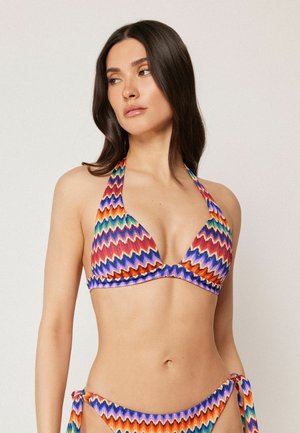 Kvinde med langt mørkt hår, iført en farverig zigzag-mønstret halterneck bikinioverdel og matchende bikinibund med bindebånd i siderne.