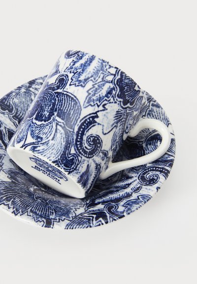 Ceramic cup and saucer set with intricate blue floral patterns on a white background. The cup has a curved handle and is slightly tilted.