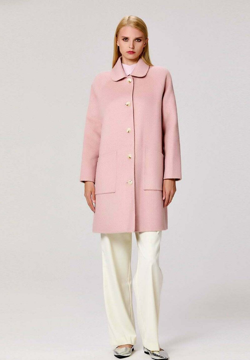 Manteau en mélange de laine rose avec un col rond, des boutons sur le devant et deux grandes poches. Assorti avec un pantalon blanc et des chaussures argentées élégantes.