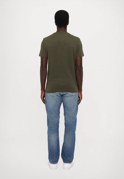 Olivgrön bomullströja med korta ärmar, matchad med ljusblå jeans och vita sneakers, sedd bakifrån.