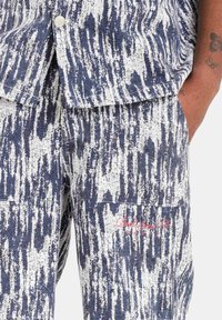 Blauwe en witte geblokte broek van denimstof, met een zak en rode geborduurde branding aan de zijkant. Geweven met verticale strepen.