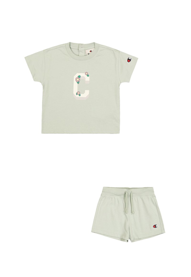 Camiseta de algodón verde claro con mangas cortas, que presenta un gran diseño de la letra "C" con acentos florales. Combinada con pantalones cortos con cordón a juego.