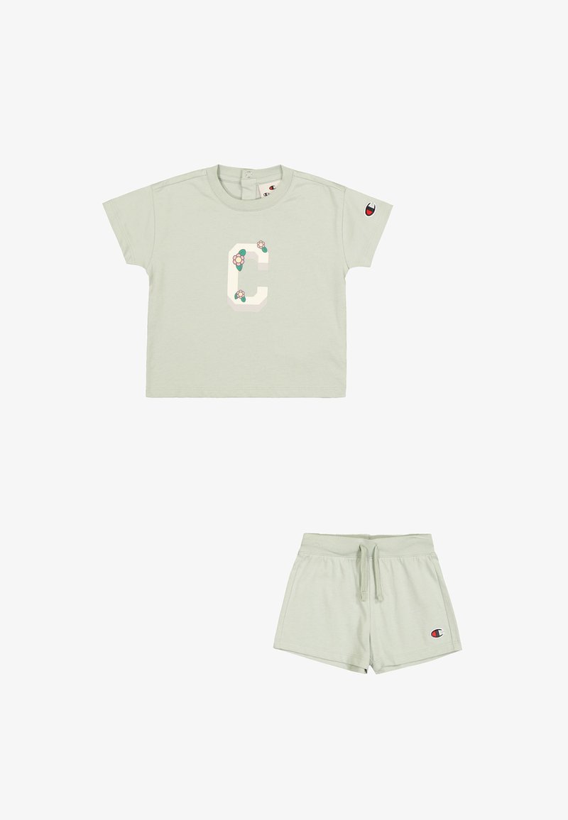 Jasnozielona bawełniana koszulka z krótkim rękawem, z dużym wzorem litery "C" ozdobionym kwiatami. W połączeniu ze spodniami na sznurku w tym samym kolorze.