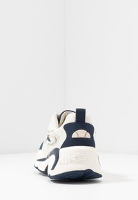 Sneaker bianco e blu navy con tomaia in rete testurizzata, colletto imbottito, accenti del logo e un tacco dal design distintivo.