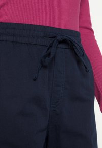 Pantalones azul marino con cintura elástica y cordón, con una textura suave y bolsillos laterales. Combinados con una blusa de manga larga rosa con textura acanalada.