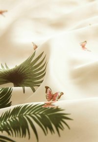 Jasno beżowa tkanina z zielonymi palmami i różowymi motylami. Gładka tekstura z opadającym krojem, podkreślająca szczegółowe nadruki botaniczne.