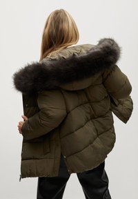 Oliwkowa kurtka puchowa z czarnym kapturem wykończonym futrem oraz z zamkiem błyskawicznym z przodu, z pikowanymi sekcjami i elastycznymi mankietami.
