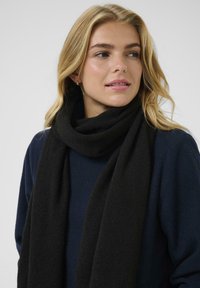 Schwarzer Schal aus weichem, strukturiertem Stoff, der um den Hals gewickelt ist, kombiniert mit einem marineblauen Oberteil. Einfaches Design ohne sichtbare Muster oder Akzente.