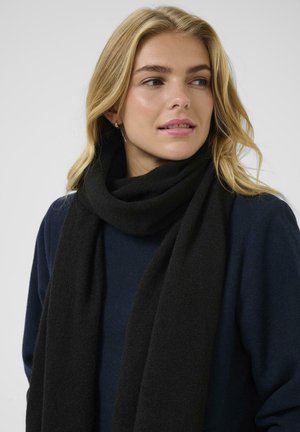 Écharpe noire en tissu doux et texturé, enroulée autour du cou, associée à un haut bleu marine. Design simple sans motifs ni accents visibles.