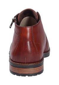 Botte en cuir marron à la cheville vue de l'arrière, avec des coutures visibles, une fermeture éclair latérale et une semelle en bois stratifiée avec un profil en caoutchouc noir.